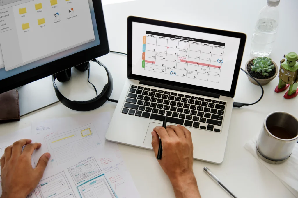 Persona planificando tareas en calendario digital con laptop.