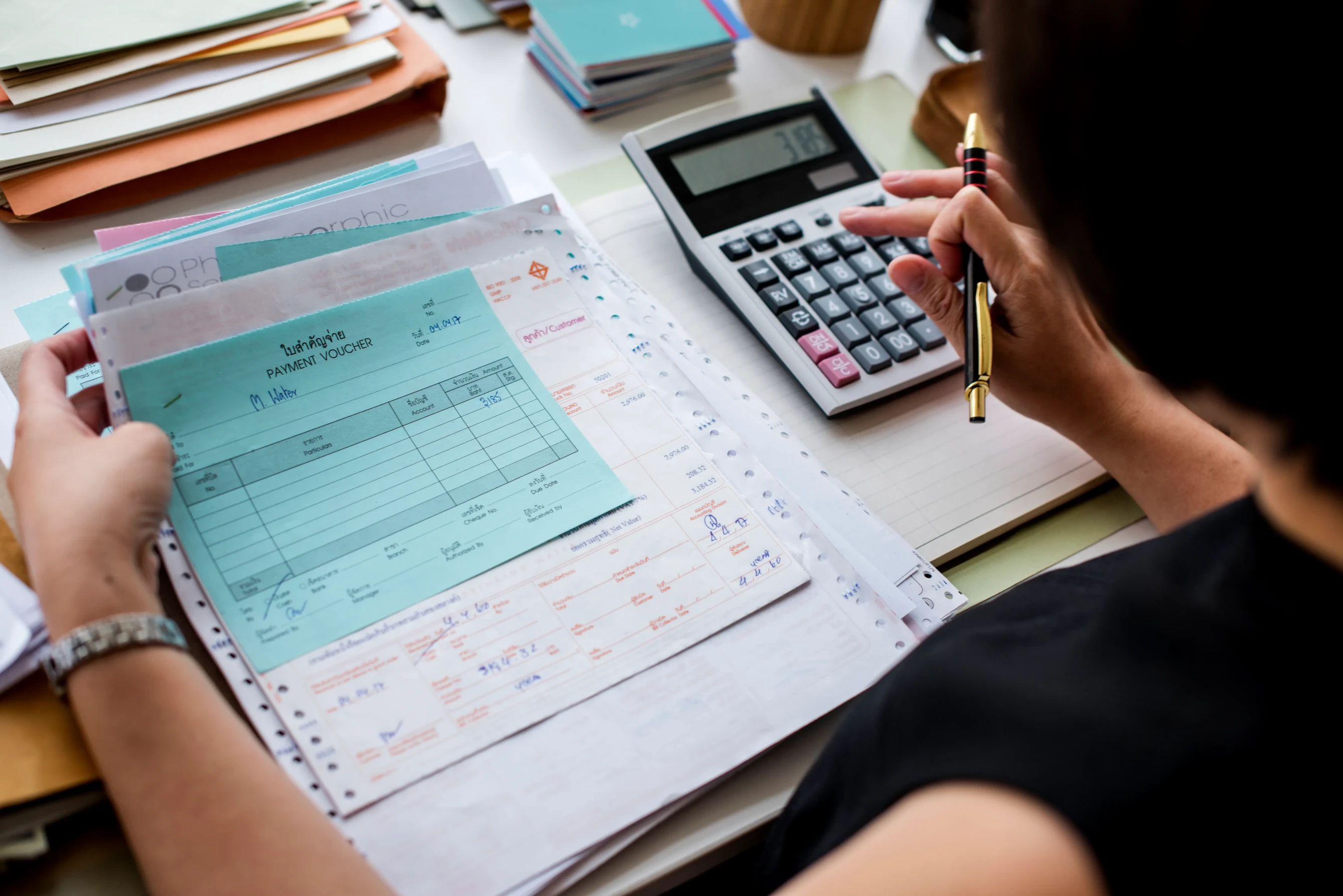 Mujer calculando facturas con calculadora y bolígrafo.