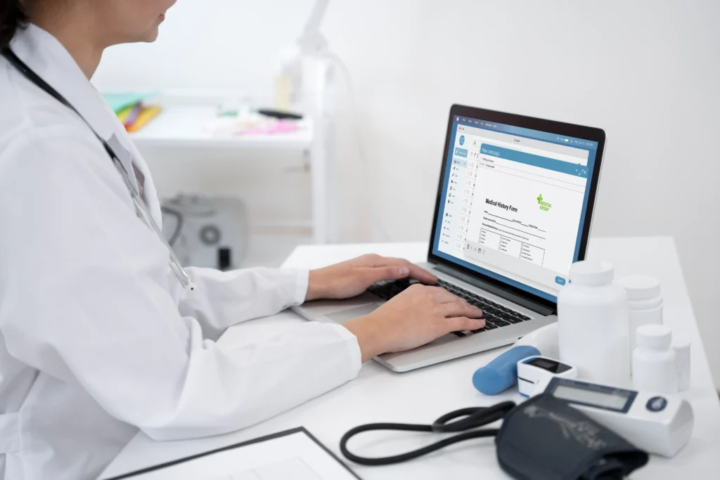 Médico trabajando en laptop con registros médicos electrónicos.
