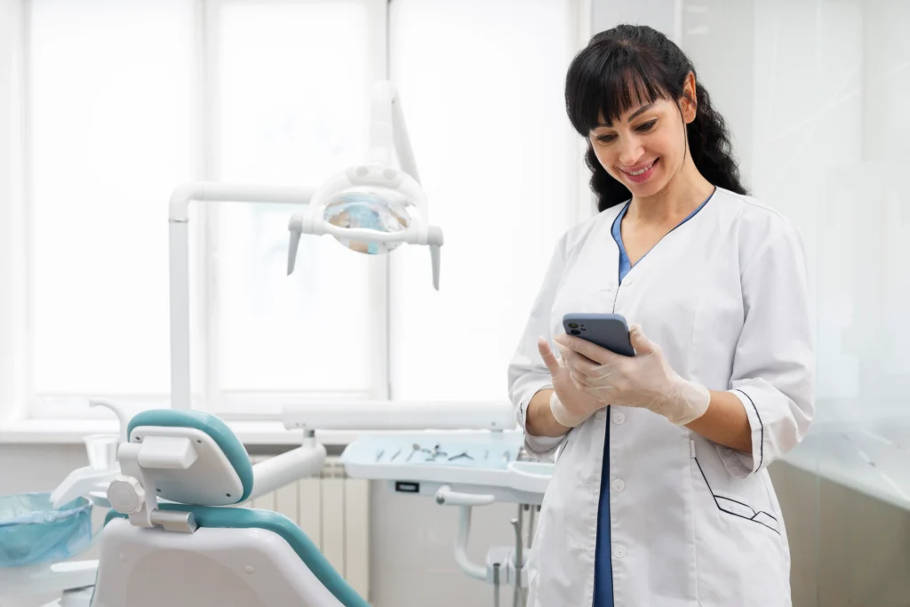 dentista sonriendo mientras usa su teléfono en clínica dental