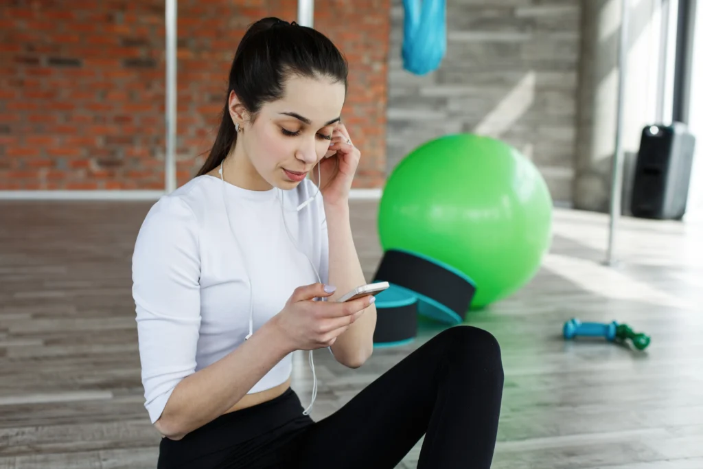 Mujer en gimnasio usando teléfono con auriculares.