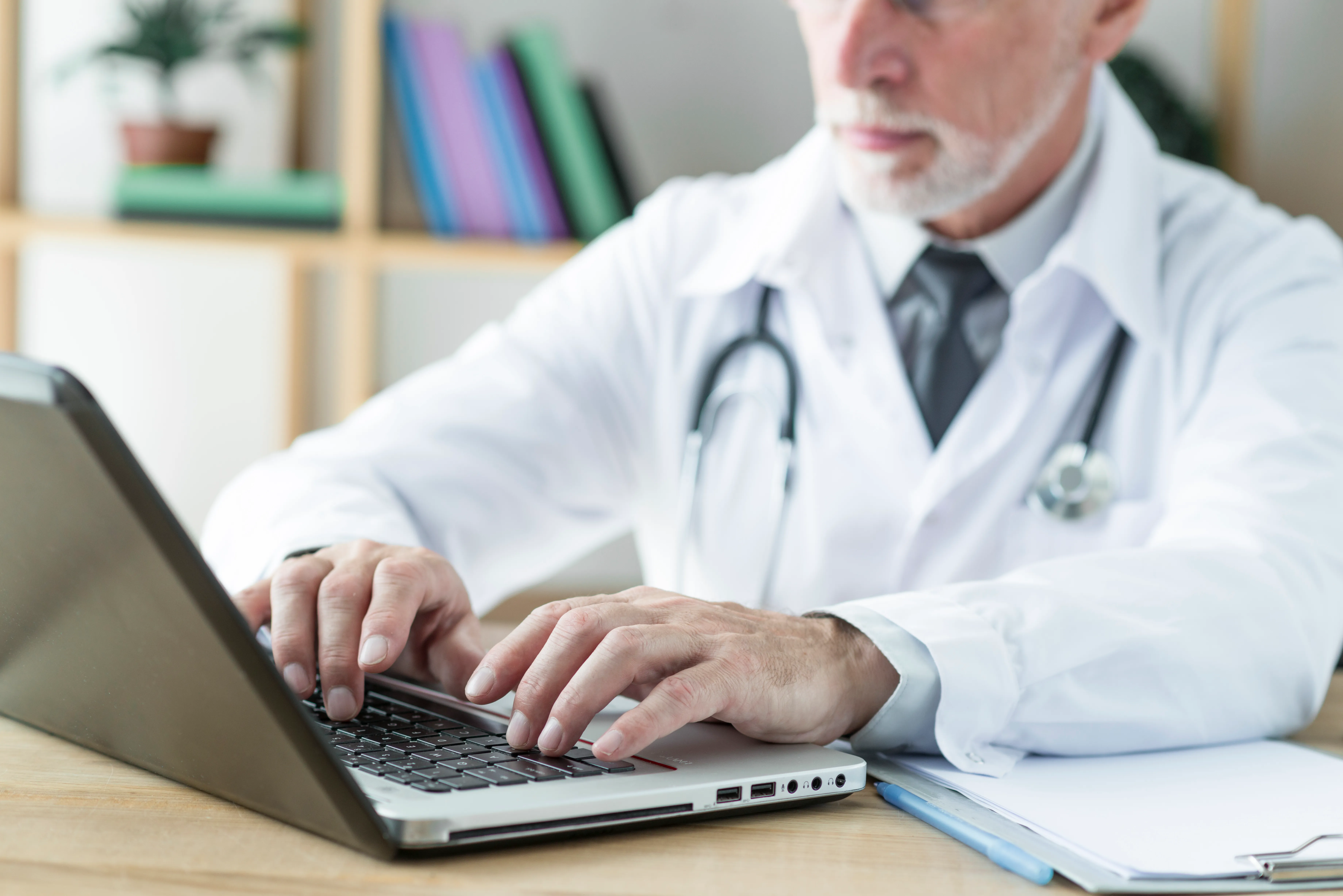 Médico escribiendo en un portátil en su consulta